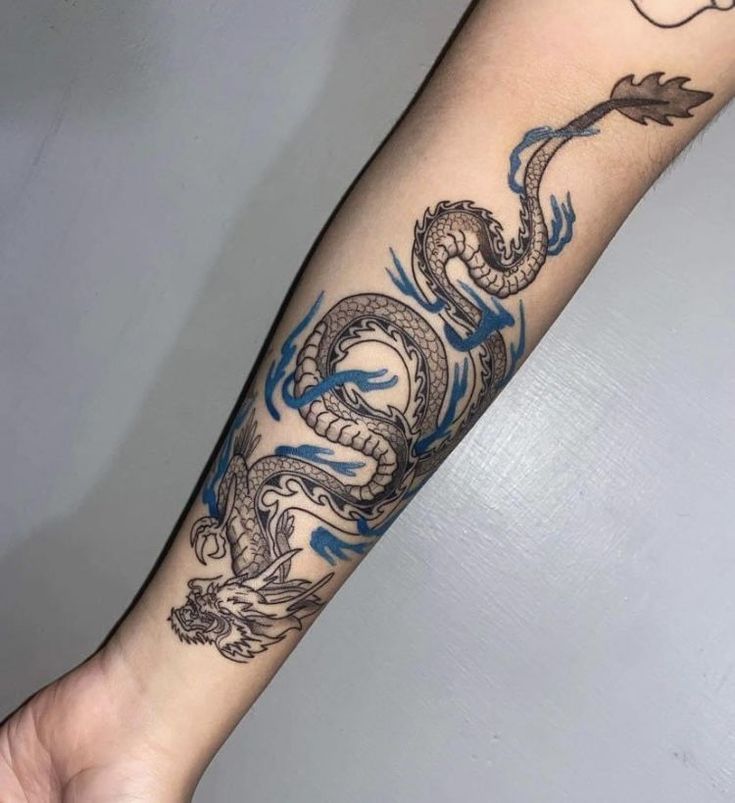 a tattoo on the arm of a person with a blue dragon and an arrow in it