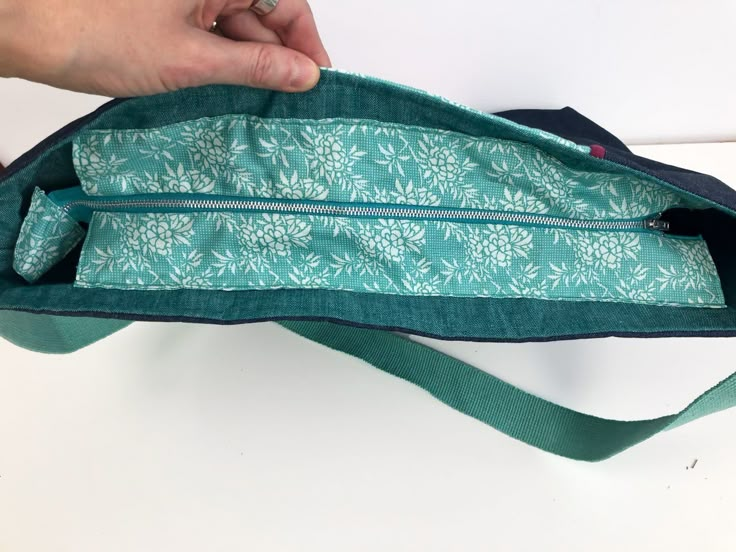 a person is opening the zipper on a green and blue bag that has flowers all over it