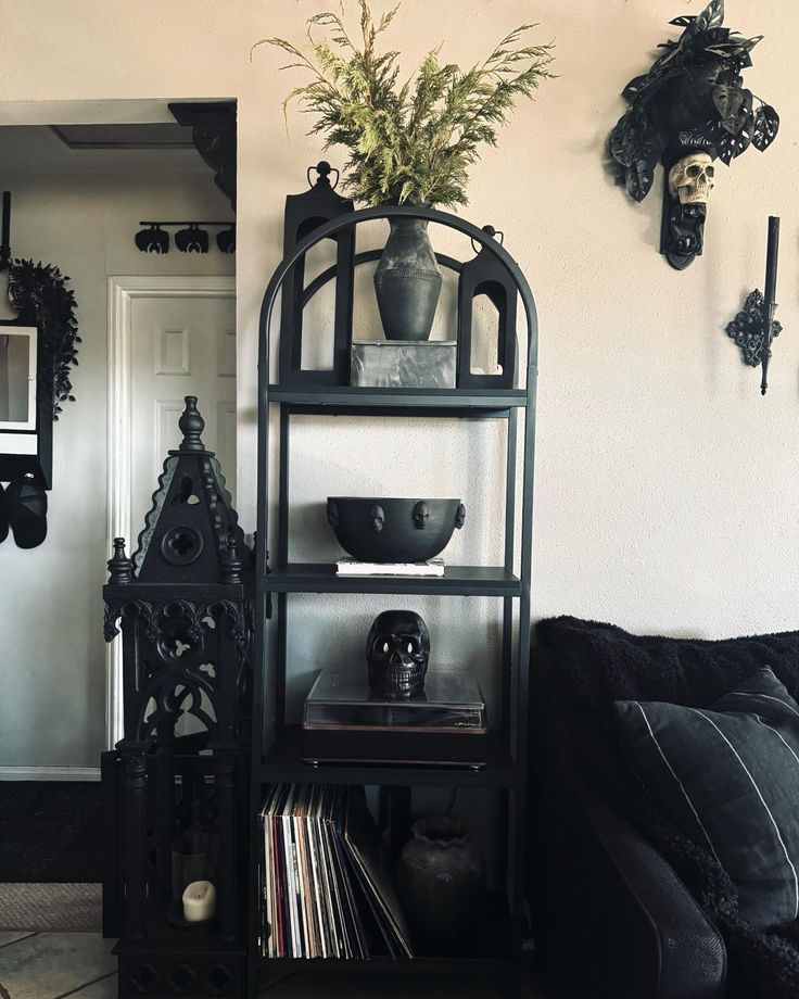 a living room with a black couch and some plants on a shelf in the corner