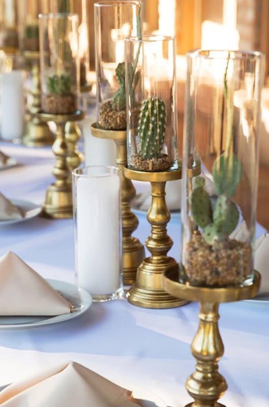 a table set with candles, plates and succulents in glass vases