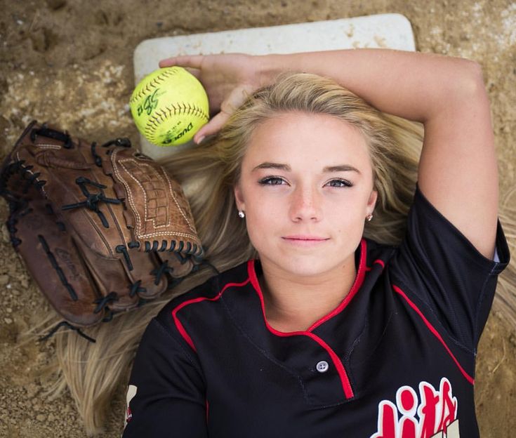 a woman laying on the ground with a baseball and glove next to her, looking up at the camera