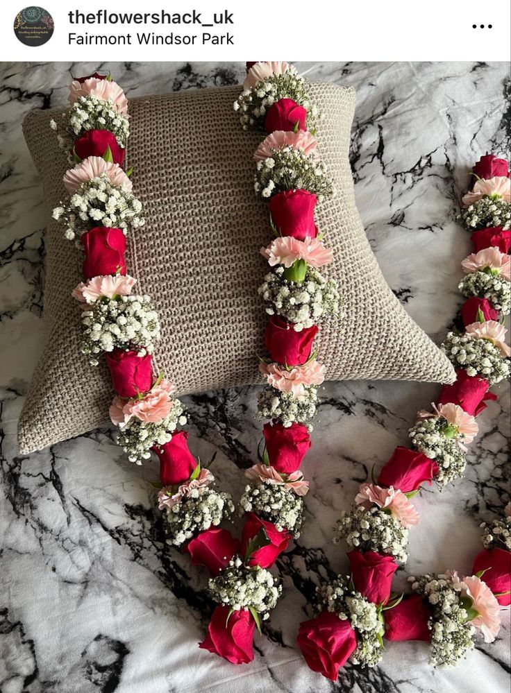 red and white flowers are attached to a pillow on a marble counter top, along with two matching necklaces