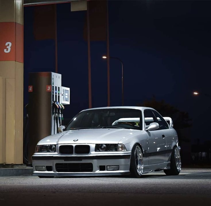 a silver car is parked in front of a gas station at night with its lights on