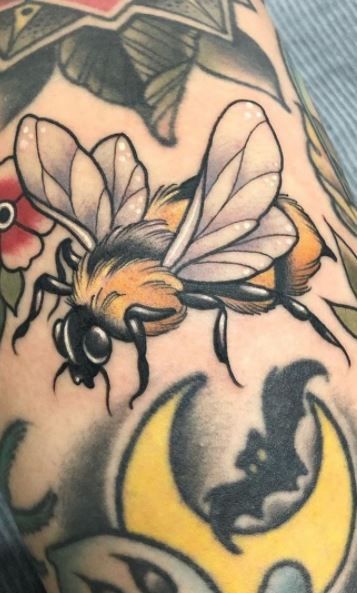 a man's arm with tattoos on it and a bee flying over the moon