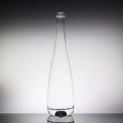 a clear glass bottle sitting on top of a reflective surface in front of a white wall