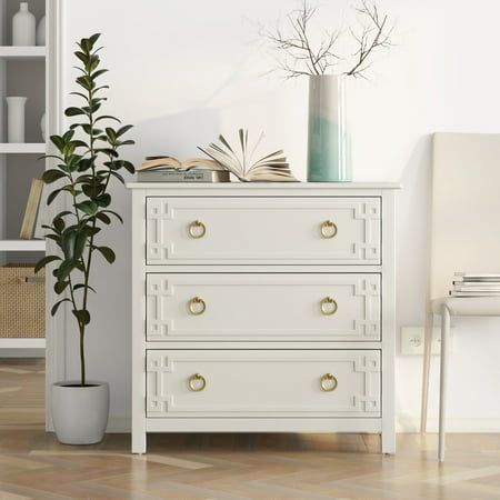 a white dresser sitting next to a tall plant in a room with books on it