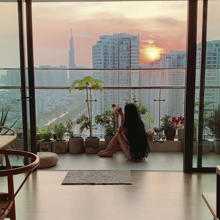 a woman sitting on top of a wooden floor next to a window filled with potted plants