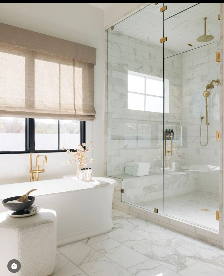 a white bathroom with gold fixtures and marble flooring, along with a walk - in shower