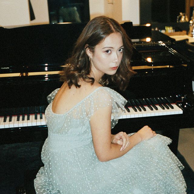 Laufey, a petite woman with short brown hair sits with her back turned to the camera. She is seated at a piano bench in front of a shiny grand piano, and looking over her shoulder in a nonchalant, casual manner. She is appears to be backstage before a concert, and is performance ready in a ruffly light blue gown. Me Core, Dara Kpop, Chappell Roan, Song Artists, How To Pose, Fav Celebs, My Favorite Music, Her Music, Cutie Patootie