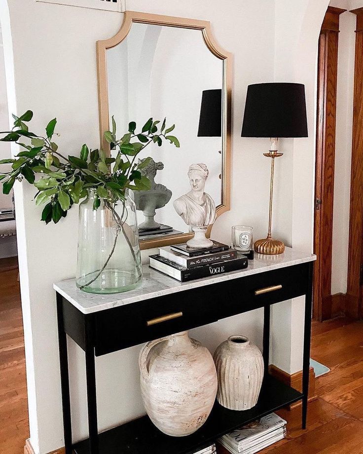 a table with two vases and a mirror on top of it next to a lamp