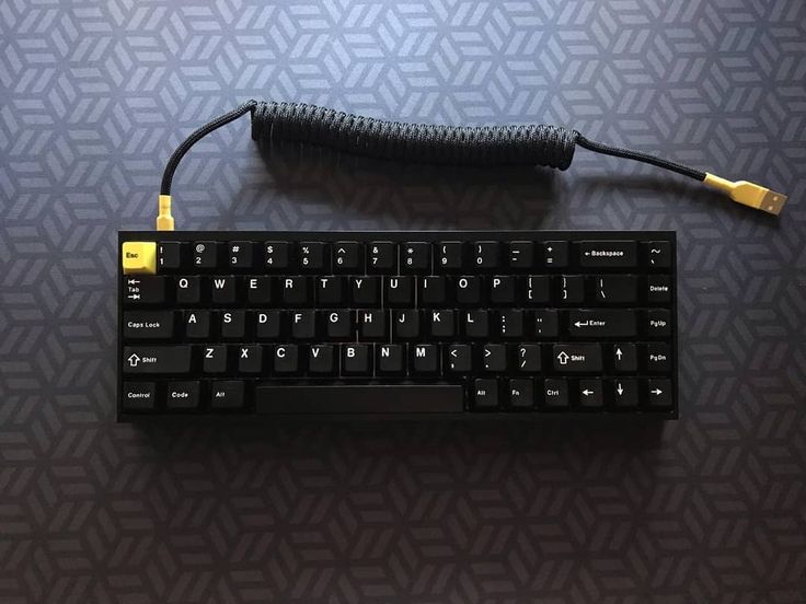 a black keyboard with yellow keys sitting on top of a blue table next to a charger