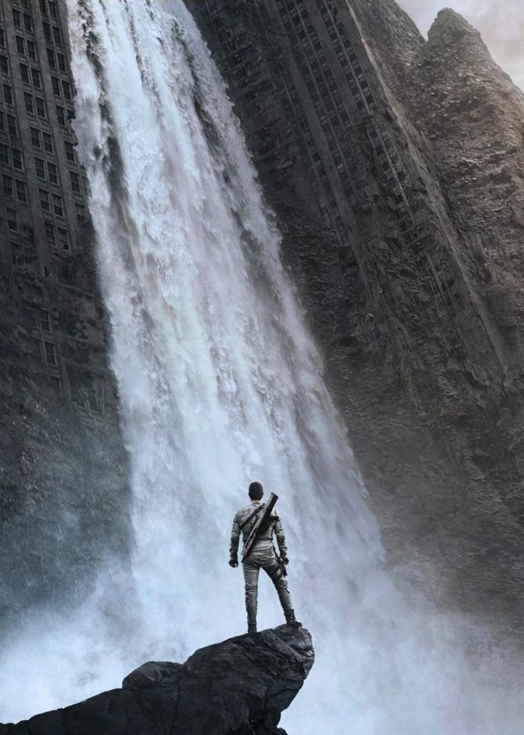 a man standing on top of a cliff next to a waterfall