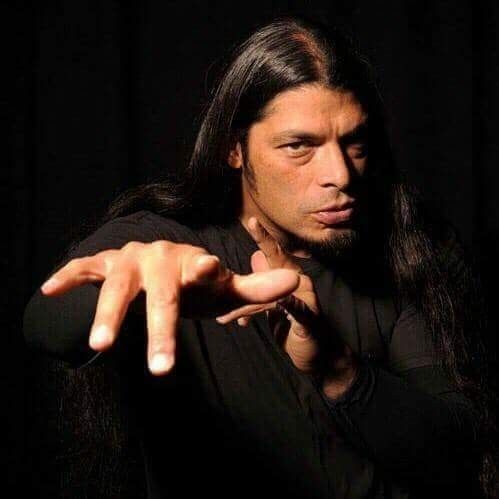 a man with long hair pointing to the side while standing in front of a black background