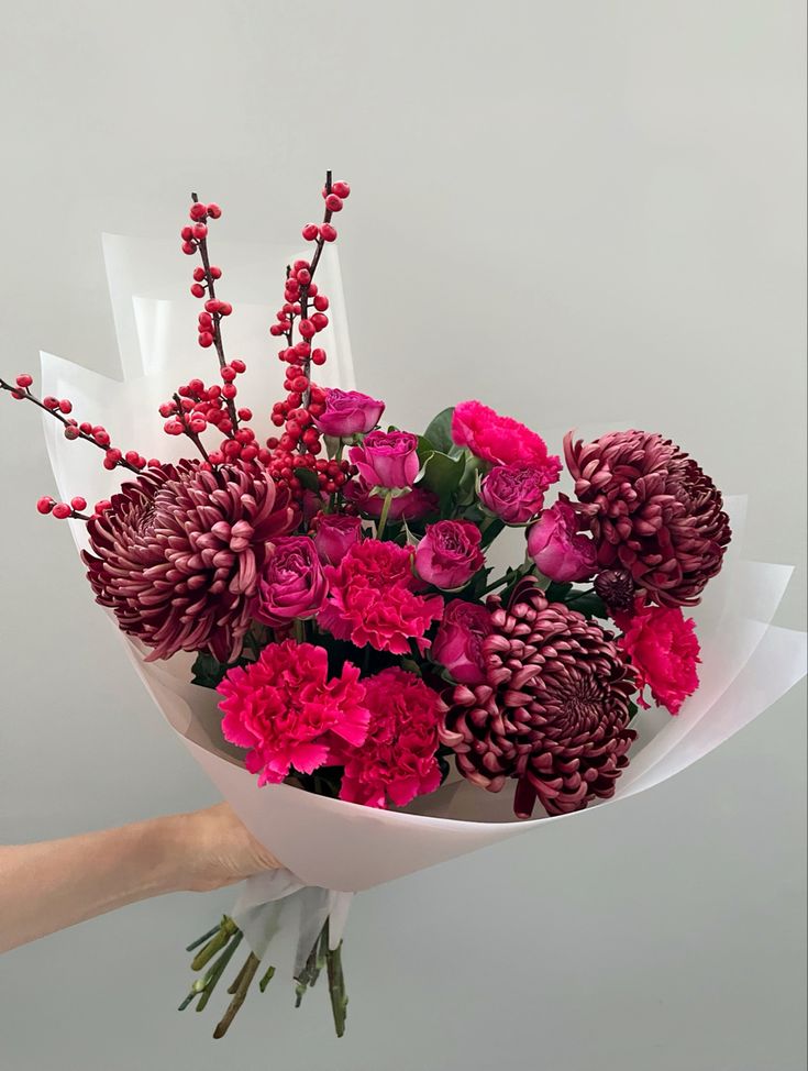 a bouquet of flowers is being held by a person's hand in front of a white wall