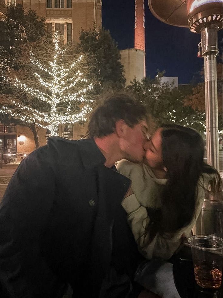 a man kissing a woman on the cheek in front of a building with christmas lights