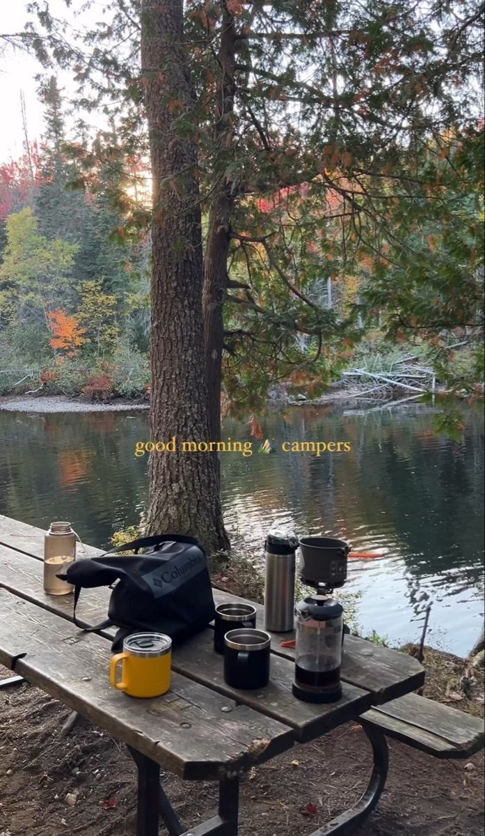 a picnic table with food on it next to a lake and trees in the background