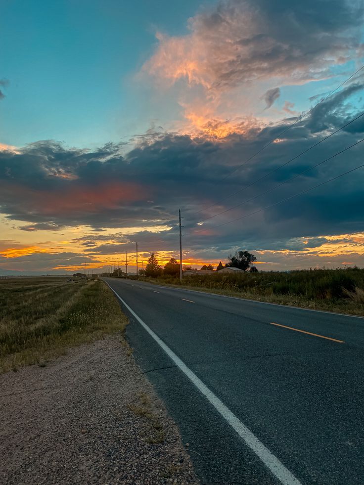 the sun is setting on an empty road in the middle of nowhere with power lines and telephone poles