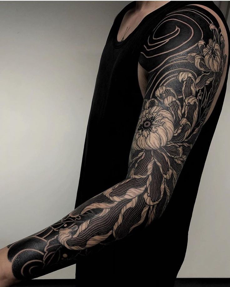 a man's arm covered in black and white tattoos with flowers on the arm