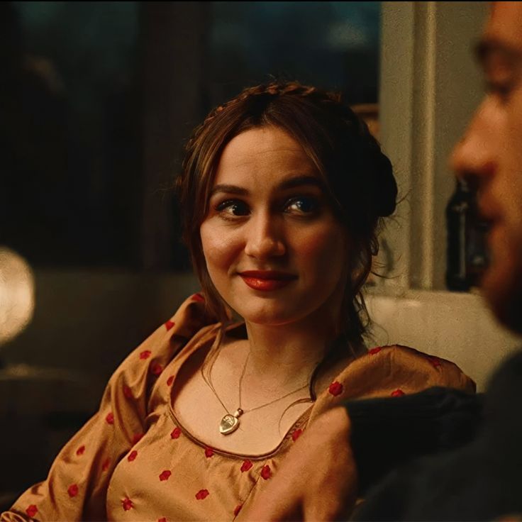 a woman sitting next to a man in front of a window wearing a brown shirt