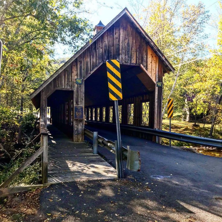 a wooden covered bridge with yellow and black striped traffic signs on it's sides