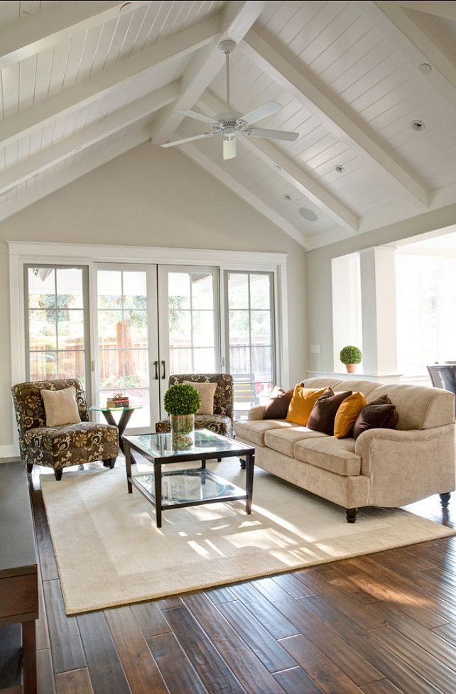 a living room filled with furniture next to a wooden floor and white walls, covered in windows