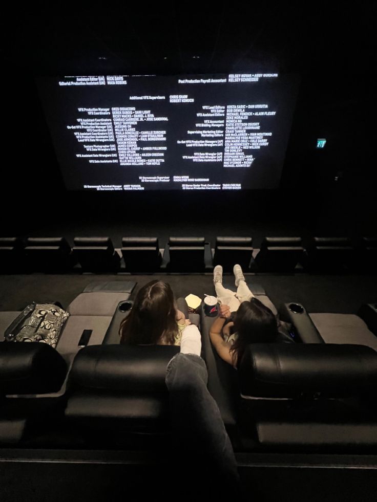 two people sitting on black couches in front of a large screen with words written on it