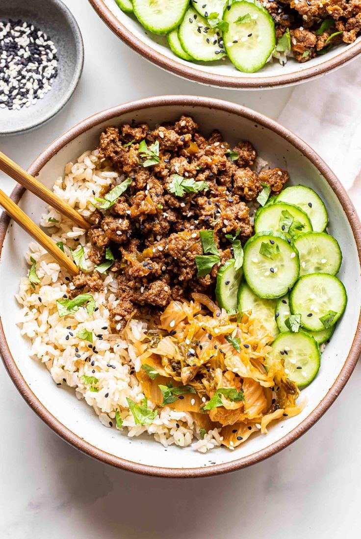 two bowls filled with rice, meat and cucumbers