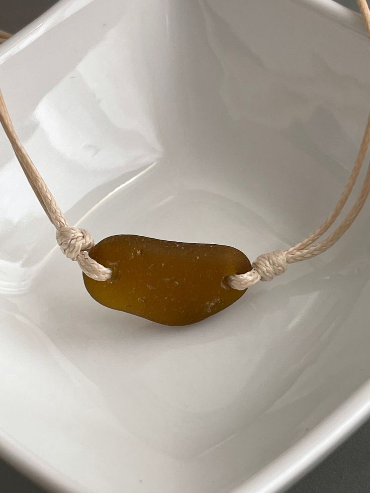 a piece of sea glass on a rope in a white square bowl with gray background