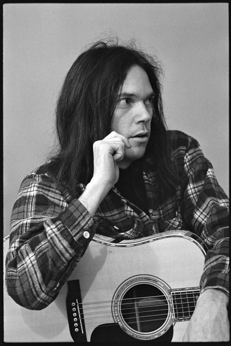 a black and white photo of a man with long hair holding an acoustic guitar in front of his face