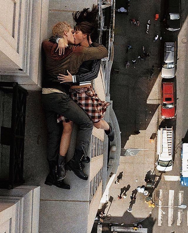 two people are kissing on the side of a building with cars and trucks in the background