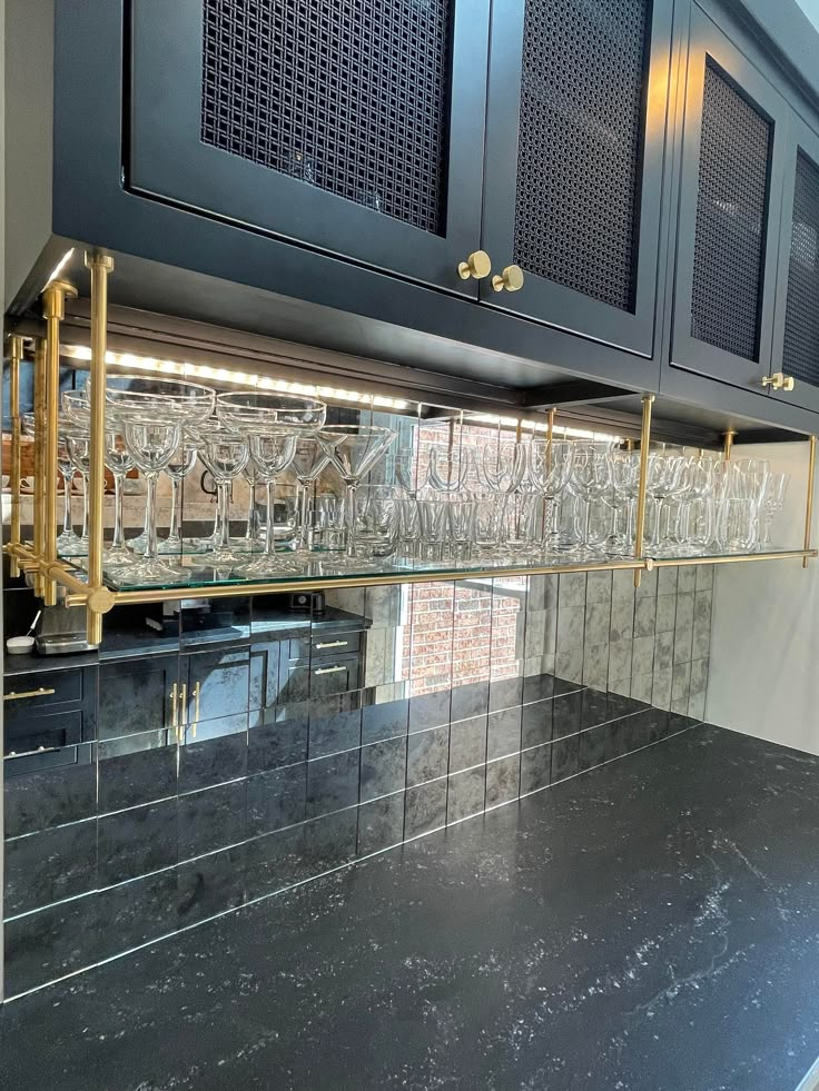 a kitchen with black counter tops and glassware on the back of the cabinetry