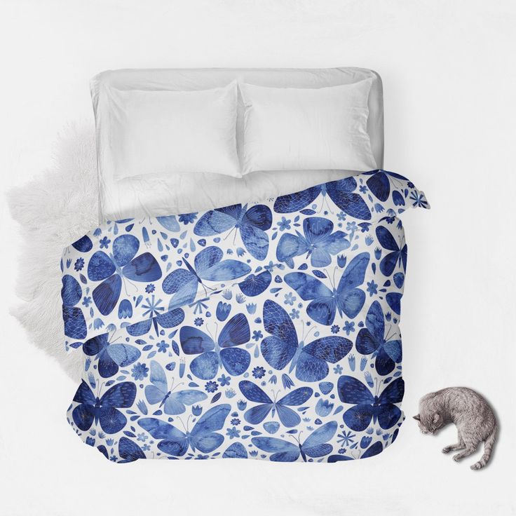 a bed with blue butterflies on it next to a white pillow and two gray cats