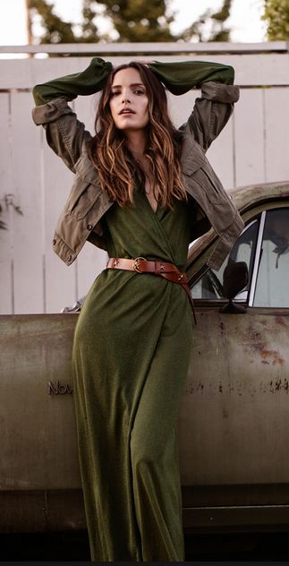 a woman standing in front of an old car with her hands on her head and arms behind her head