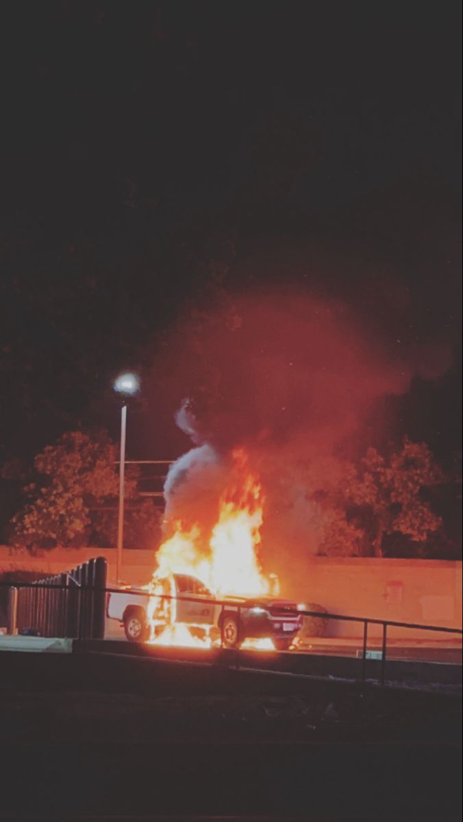 a car is on fire in front of a parking lot at night with the lights on