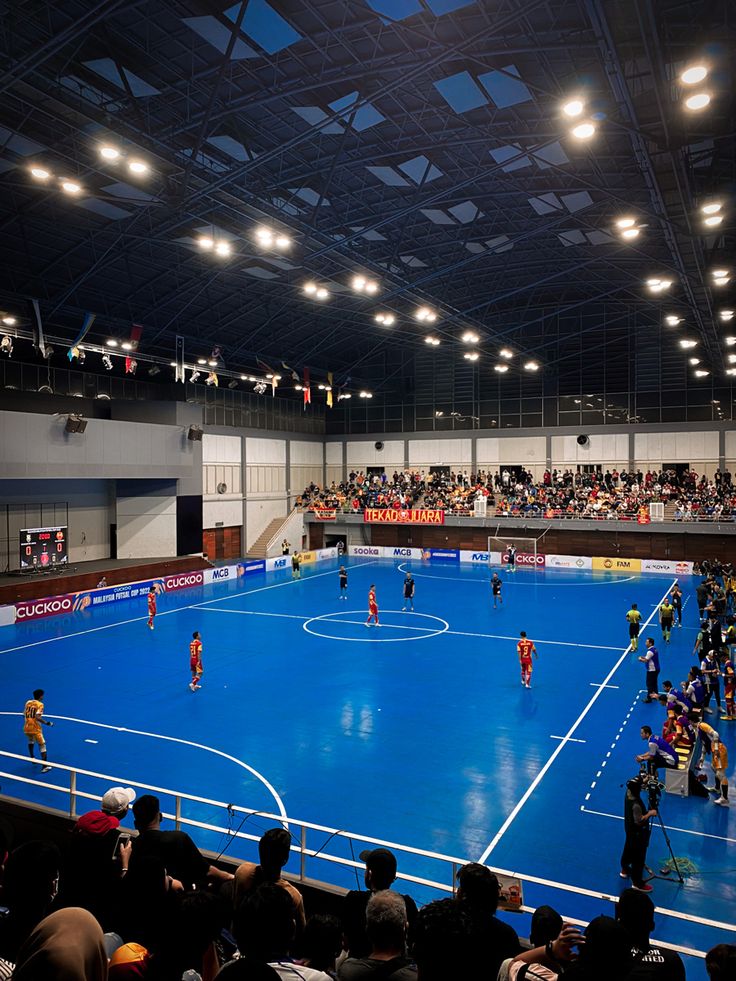 a group of people playing a game of soccer on an indoor court with fans watching