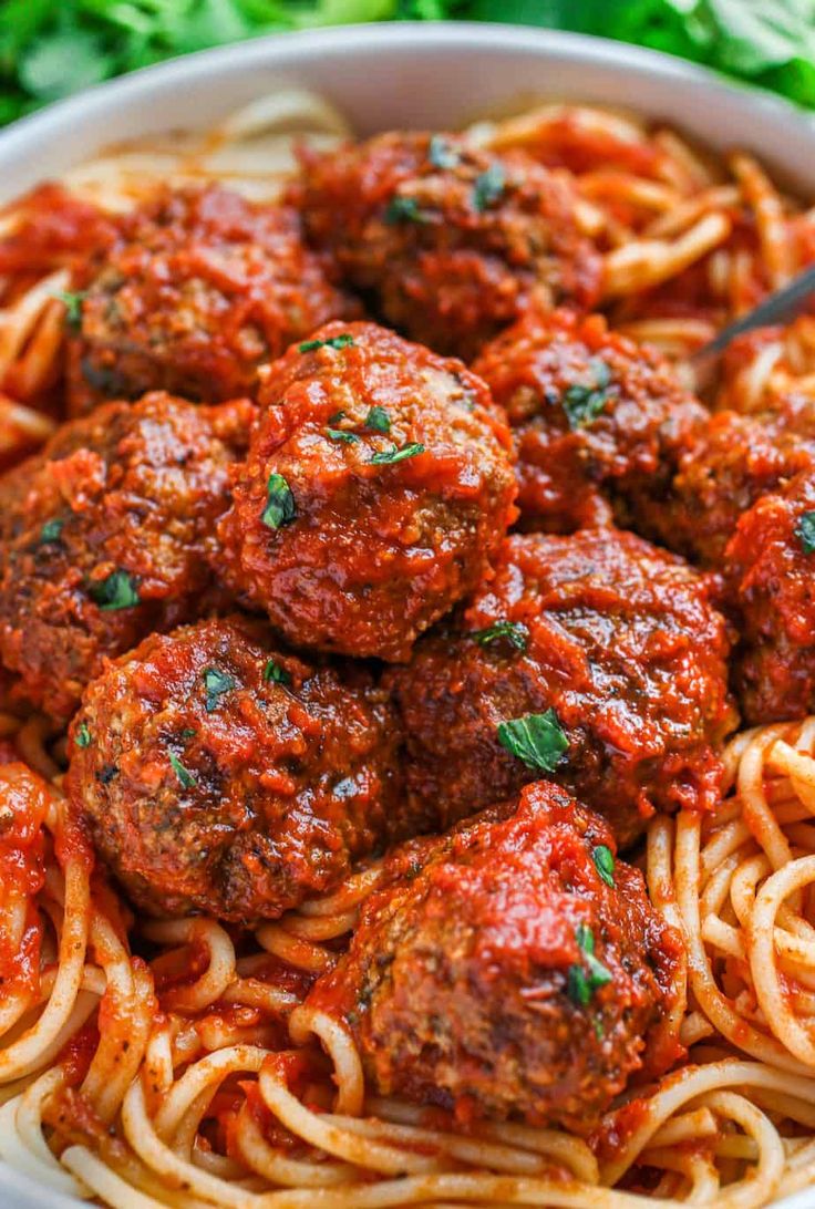 spaghetti and meatballs in a white bowl with parsley on the side, ready to be eaten