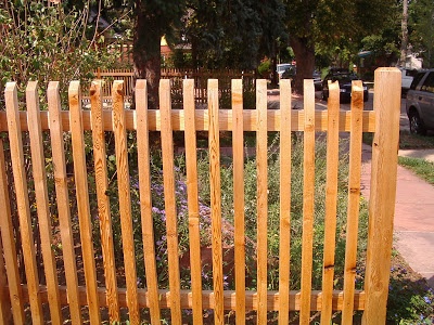 a wooden fence is shown in front of some bushes and flowers on the side walk