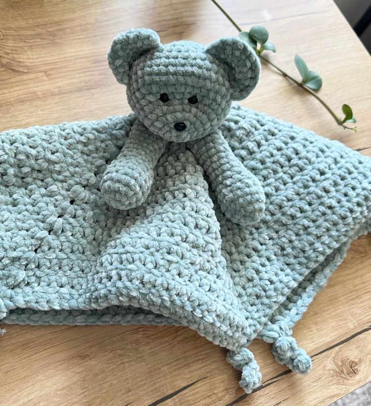 a crocheted teddy bear laying on top of a blanket