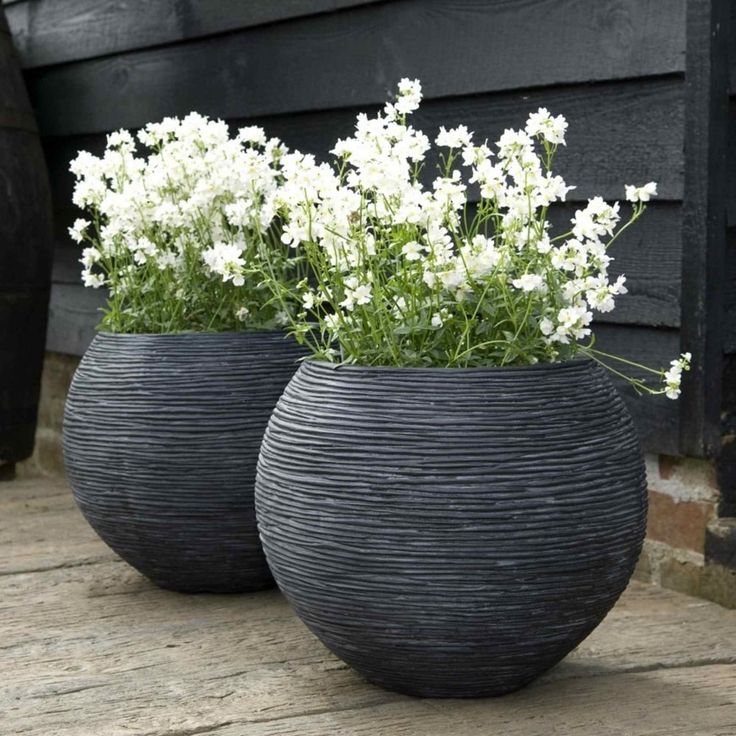 two black vases with white flowers in them sitting on a wooden table next to a building