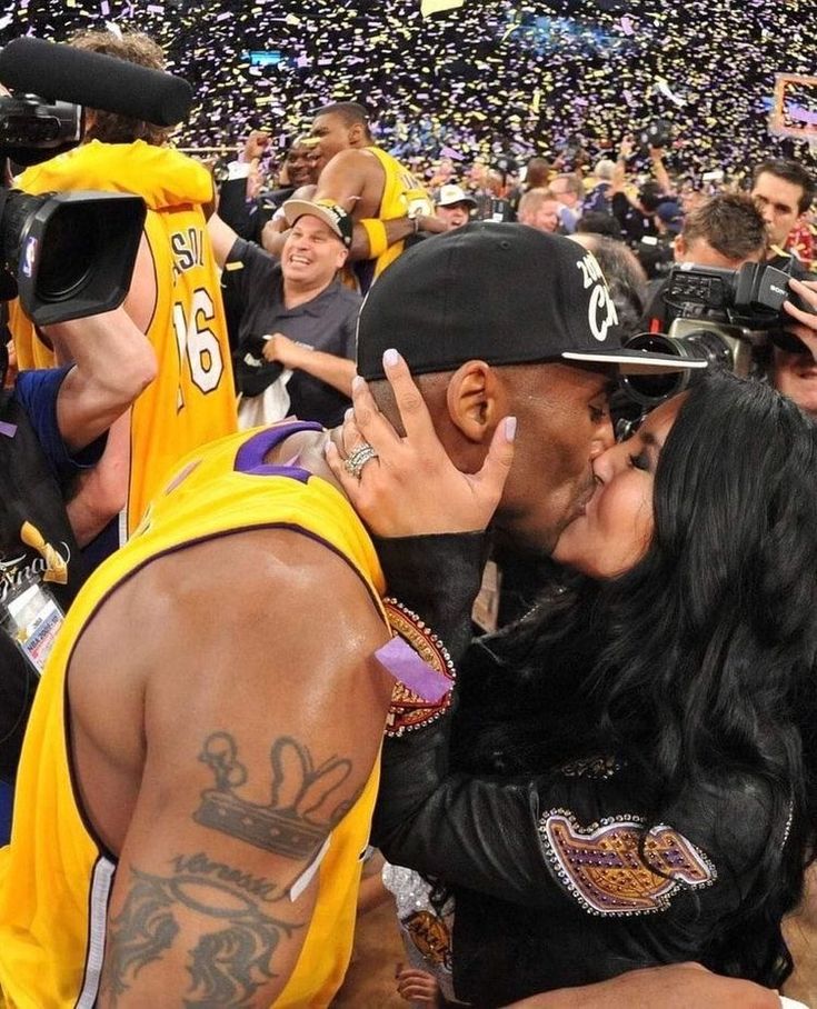 a man and woman kissing in front of a crowd at a basketball game with fans