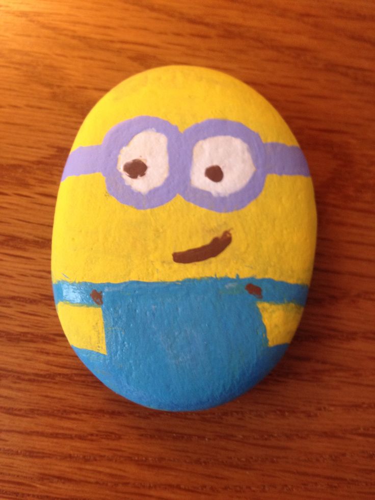 a yellow and blue painted rock with a cartoon character on it sitting on a wooden surface