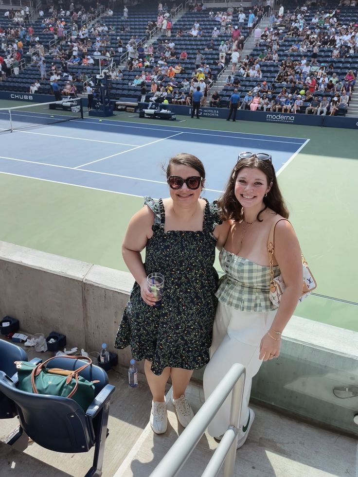 two women standing next to each other in front of a tennis court filled with people