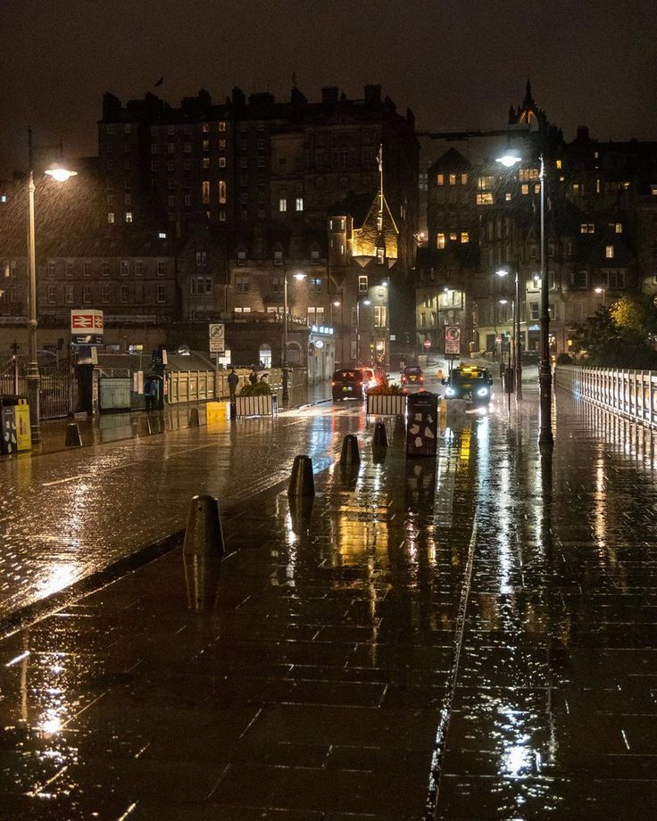 people walking in the rain at night on a city street with umbrellas and cars