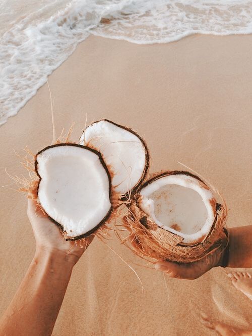 someone holding two coconuts on the beach