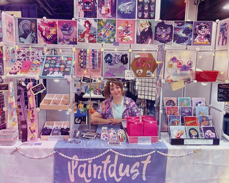 a woman sitting at a booth selling merchandise