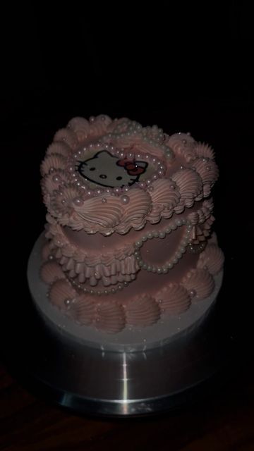 a hello kitty cake with pink icing and pearls on it's edges, sitting on a silver platter