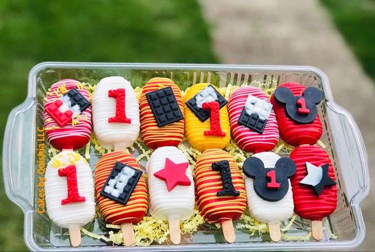 a plastic container filled with cake pops covered in mickey mouse frosting and topped with fondant