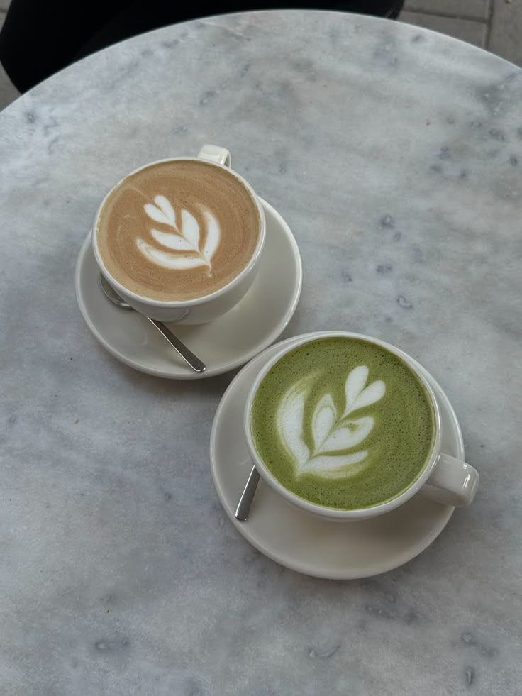 two cups of green tea with white designs on them sitting on a marble table top