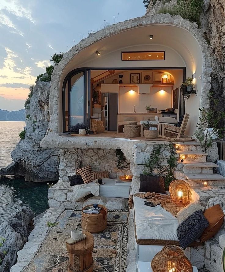 an outdoor living area next to the ocean at dusk with candles lit on the couches