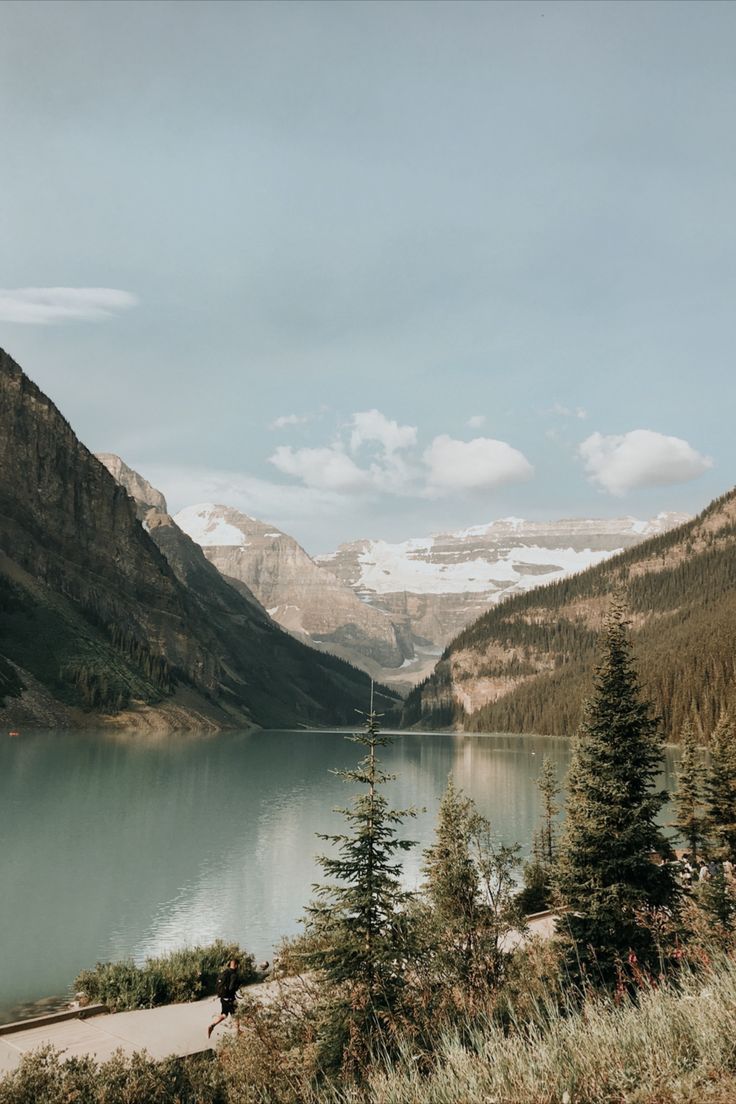 a lake surrounded by mountains and trees on a cloudy day